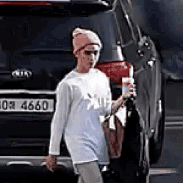a woman is walking down the street holding a drink in front of a car .