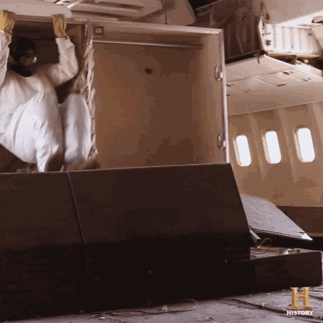 a man in a hazmat suit is loading luggage into an airplane with the letter h in the corner