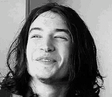 a black and white photo of a young man with long hair smiling .