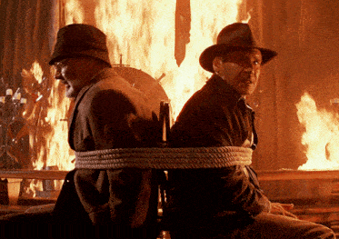 two men tied together with rope in front of a burning building