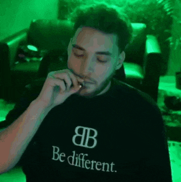 a man is smoking a cigarette while wearing a black shirt that says `` be different '' .