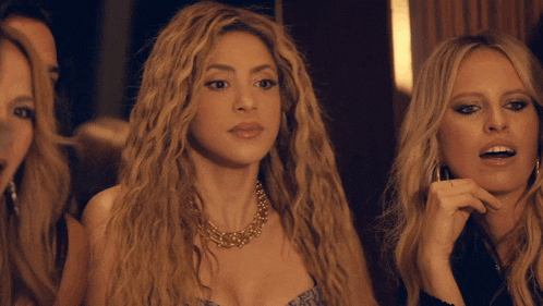 a woman with blonde hair and a gold necklace stands next to two other women