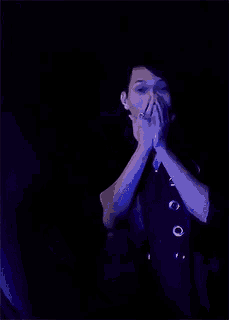 a man in a black shirt is dancing in a dark room with blue lights behind him