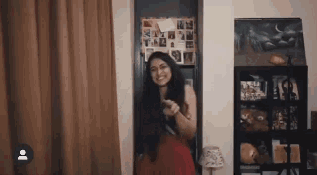 a woman in a red dress is standing in a room with a shelf .