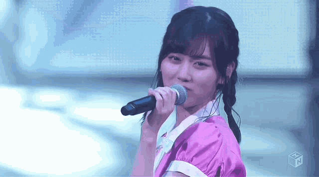a young woman in a purple dress is singing into a microphone on a stage .