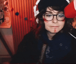 a woman wearing glasses and a hat with blood on her face looks at the camera