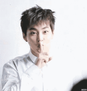 a young man in a white shirt is making a shhh gesture with his finger to his mouth .