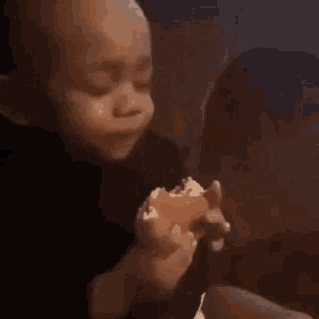 a baby is crying while eating a hamburger and making a funny face .