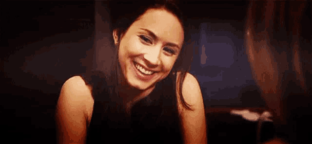 a woman is smiling at another woman while sitting at a table in a dark room .
