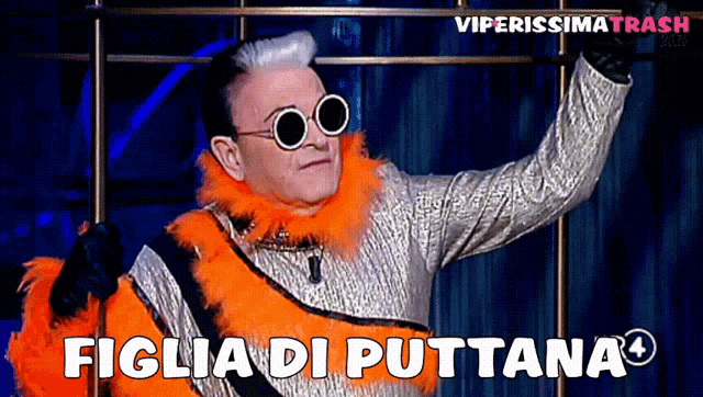 a man wearing sunglasses and an orange feather boa says " figlia di puttana "