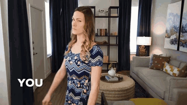 a woman in a blue dress is standing in a living room with the words " you " written in the corner