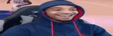a man wearing a blue hoodie is smiling while sitting in a chair .