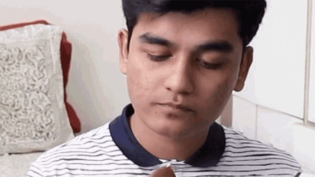 a young man in a striped shirt is eating a piece of food .