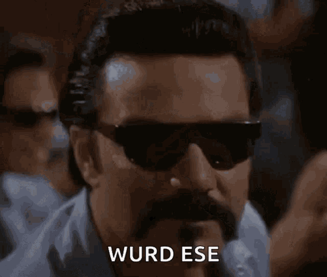 a man with a mustache and sunglasses is making a funny face and saying wurd ese .