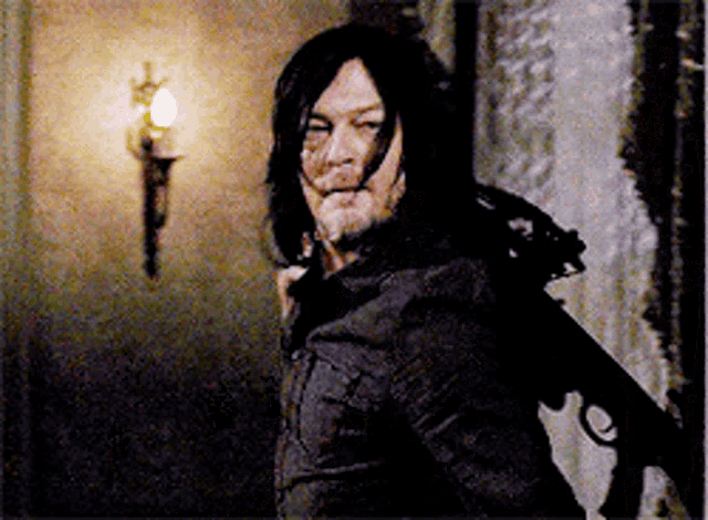 a man with long hair and a beard is standing in a dark room holding a gun