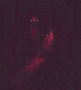 a woman sits on a bed in a dark room with red lights