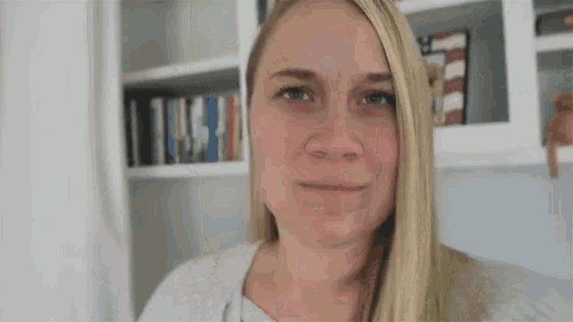 a woman with blonde hair is smiling in front of a bookshelf with books on it