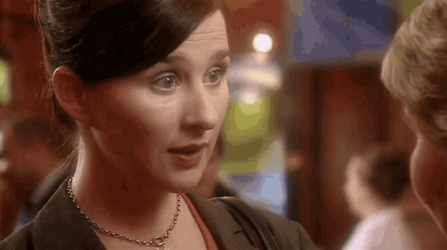 a woman wearing a necklace and a jacket looks at another woman