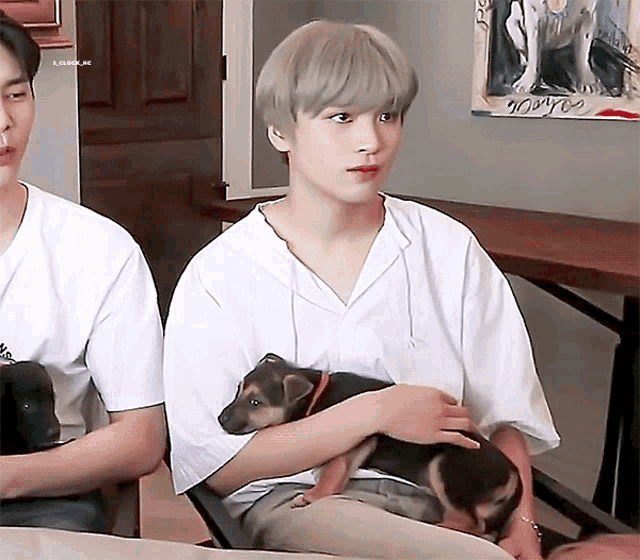 a man is holding a small dog in his arms while sitting next to another man .