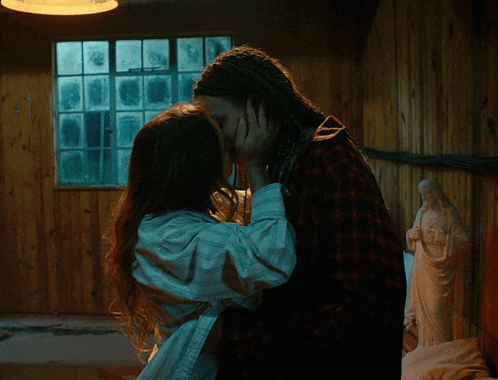 a man and woman are kissing in front of a statue of jesus