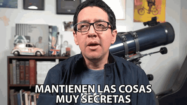 a man wearing glasses says " mantienen las cosas muy secretas " in front of a telescope
