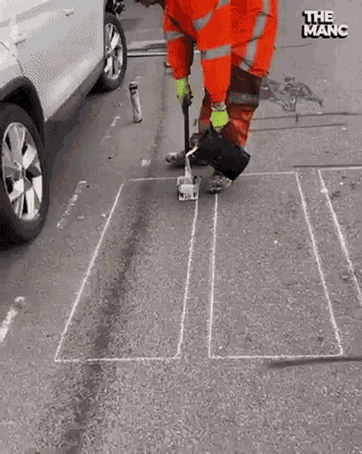 a man is drawing a square on the side of a road with chalk .
