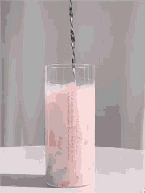 a glass of pink milkshake is being poured into a glass with a straw .