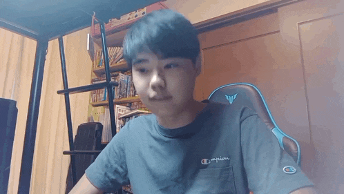 a young boy wearing a champion t-shirt is sitting at a desk in front of a computer screen .