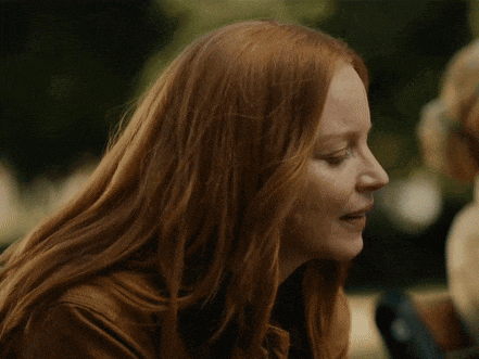 a woman with long red hair looks down at something