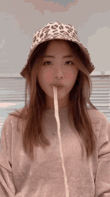 a woman wearing a bucket hat and a sweater is holding a stick in her mouth ..
