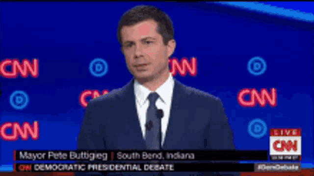 a man in a suit and tie is standing in front of a cnn screen