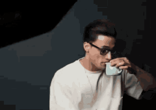 a man wearing sunglasses and a white shirt is drinking from a cup .
