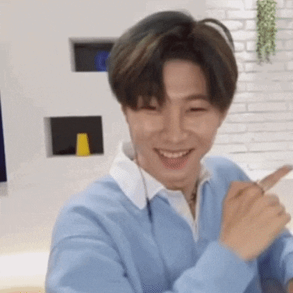a young man wearing a blue sweater and headphones is smiling and pointing at the camera .
