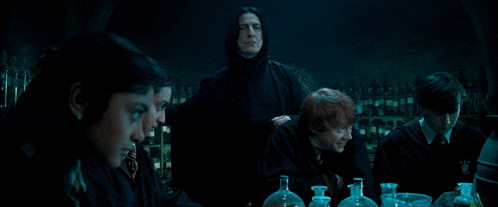 a group of people are gathered around a table with bottles and a man in a black cape standing behind them