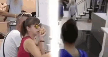 a woman is eating a sandwich while a man kisses her on the cheek in a kitchen .