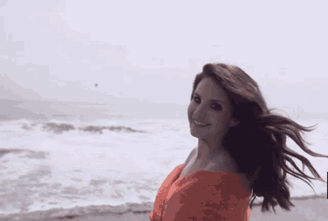 a woman in a red dress is standing on a beach with her hair blowing in the wind .