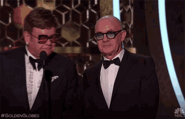 two men in tuxedos and bow ties are standing next to each other at a golden globes event