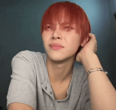 a man with red hair is wearing a grey shirt and a bracelet on his wrist .