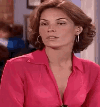 a woman wearing a pink shirt and hoop earrings is making a funny face .