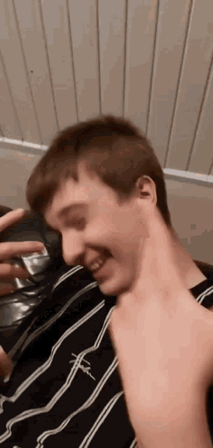 a young man in a black and white striped shirt is sitting on a couch holding a glass .