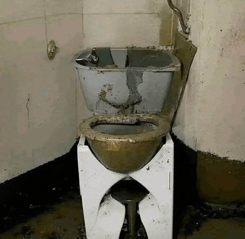 a dirty toilet in a bathroom with a bathtub in the background .