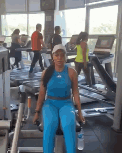 a woman in a blue tank top is sitting on a machine in a gym
