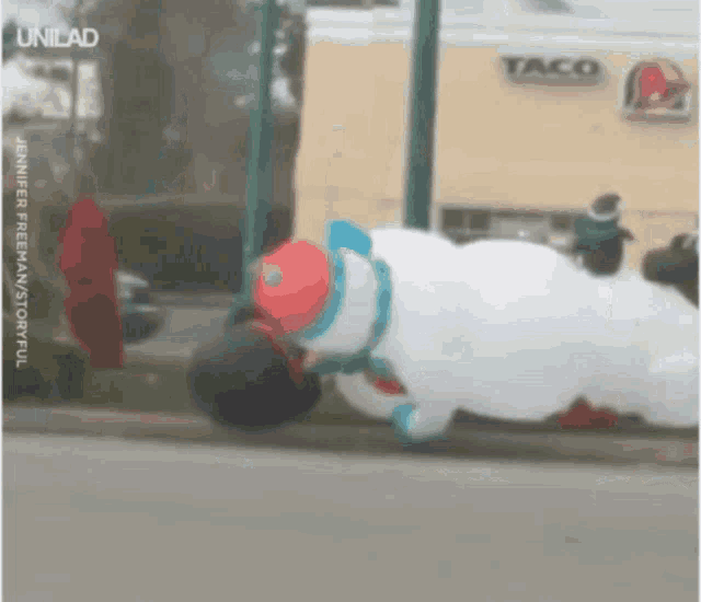 a large snowman is laying on the sidewalk in front of a taco restaurant
