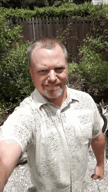 a man taking a selfie in front of a fence and bushes