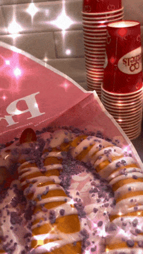 a candy cane shaped donut sits next to a stack of red cups