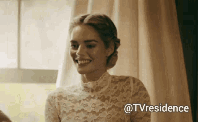 a woman in a white lace top is smiling in front of a window