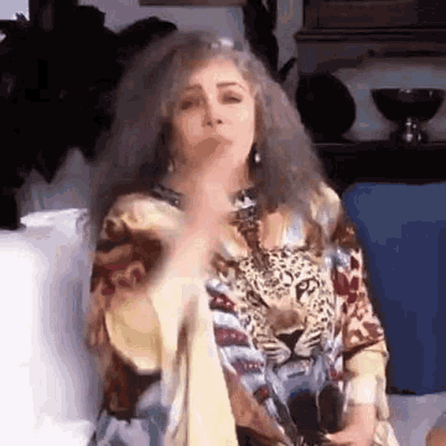 a woman with long hair is sitting on a couch in a living room wearing a leopard print shirt .