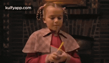 a little girl in a cape is holding a book and a fan .