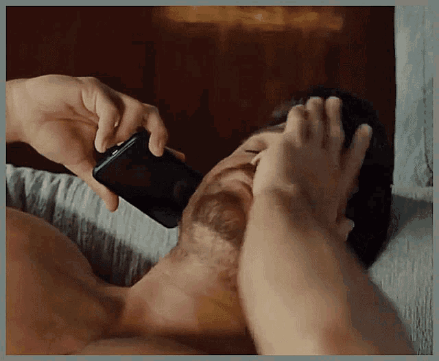 a man laying on a bed covering his face with his hand while holding a cell phone