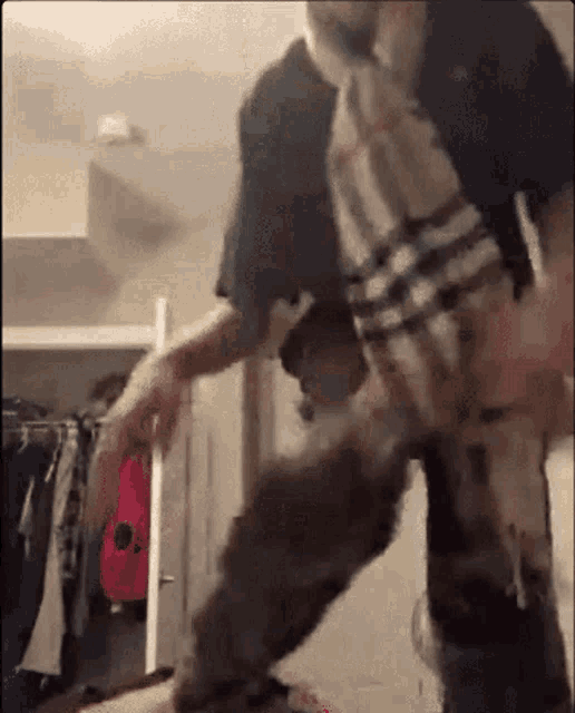 a man wearing a plaid shirt is standing in a closet